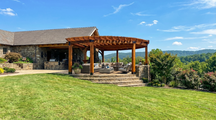 Outdoor patio area with Big Timber wooden pergola and stone walls, surrounded by greenery and mountains.